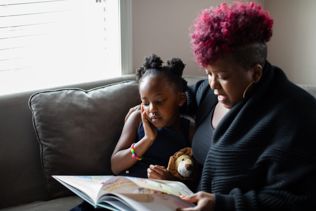mother and daughter reading book together on coach