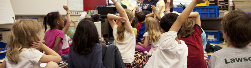 A diverse classroom of children being read to by the teacher.