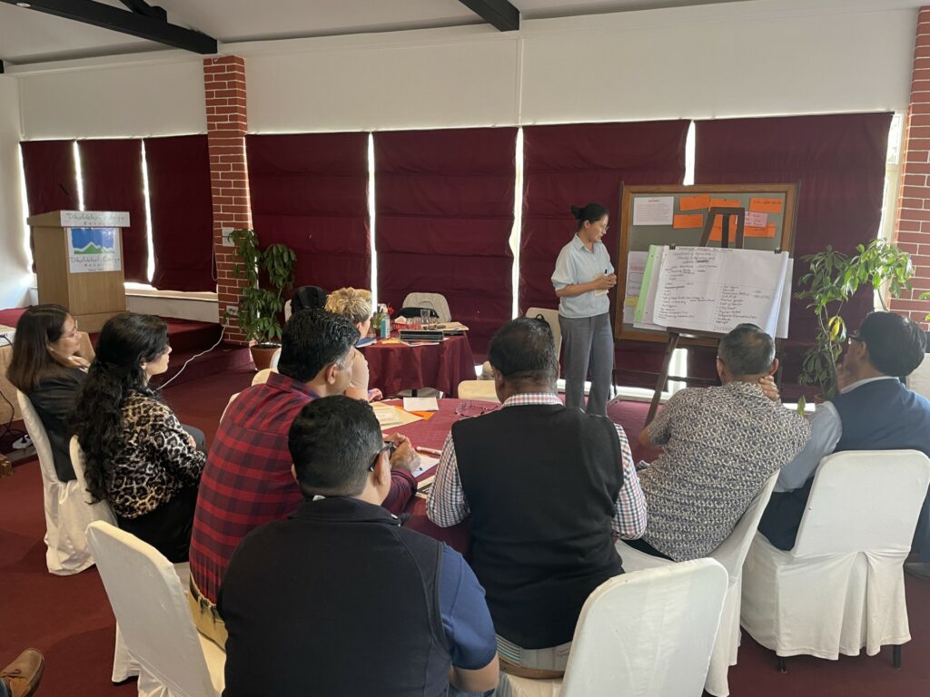 A break out group at the policy workshop. Nine participants are seated around a table and a woman stands and makes notes on a flipchart.