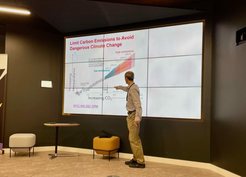 A man pointing at a large screen displaying the text 'Limit Carbon Emissions to Avoid Dangerous Climate Change' and a graph.