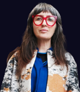 A portrait image of Cristina Cerulli wearing an electric blue shirt and red glasses